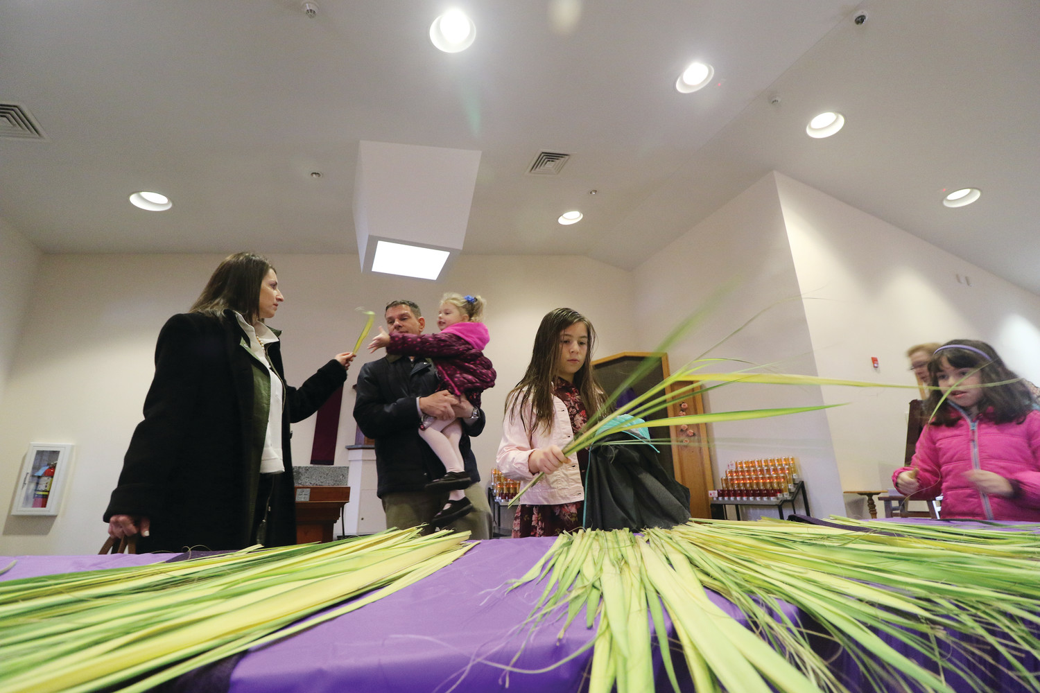 Parishioners reach for palm fronds after arriving for Palm Sunday Mass March 25 at St. Theresa Church in Tiverton.